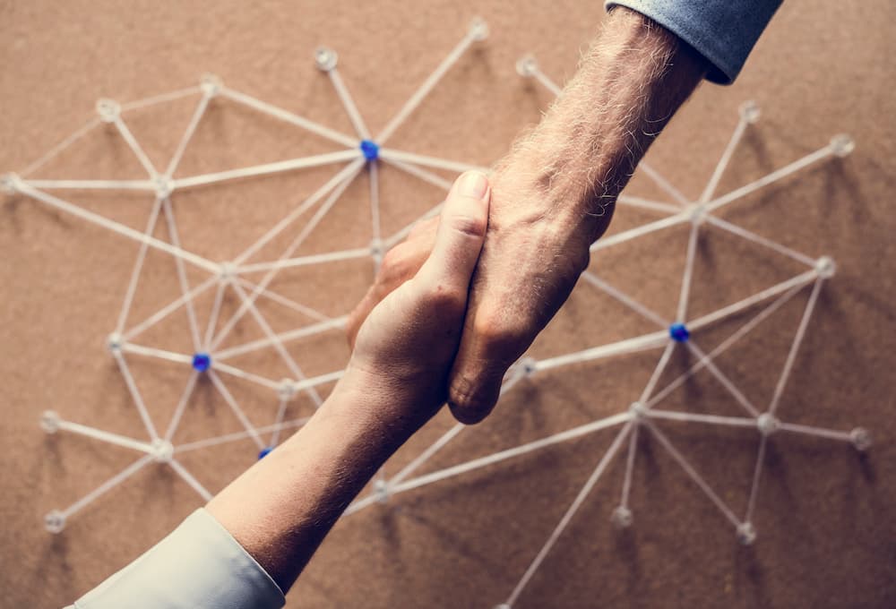 Two hands engaged in a handshake against a background of connected white string showing human connection.